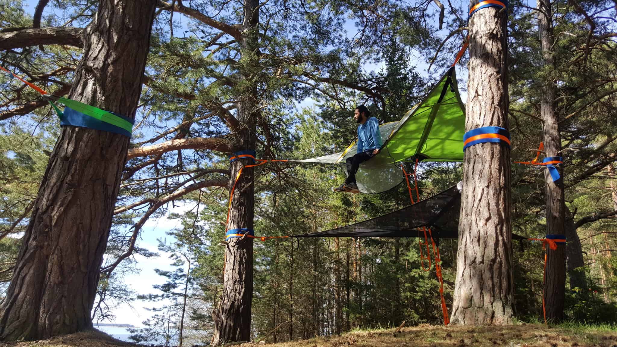 Kuvassa henkilö istuu puuhun kiinnitetyssä Tentsile-teltassa.