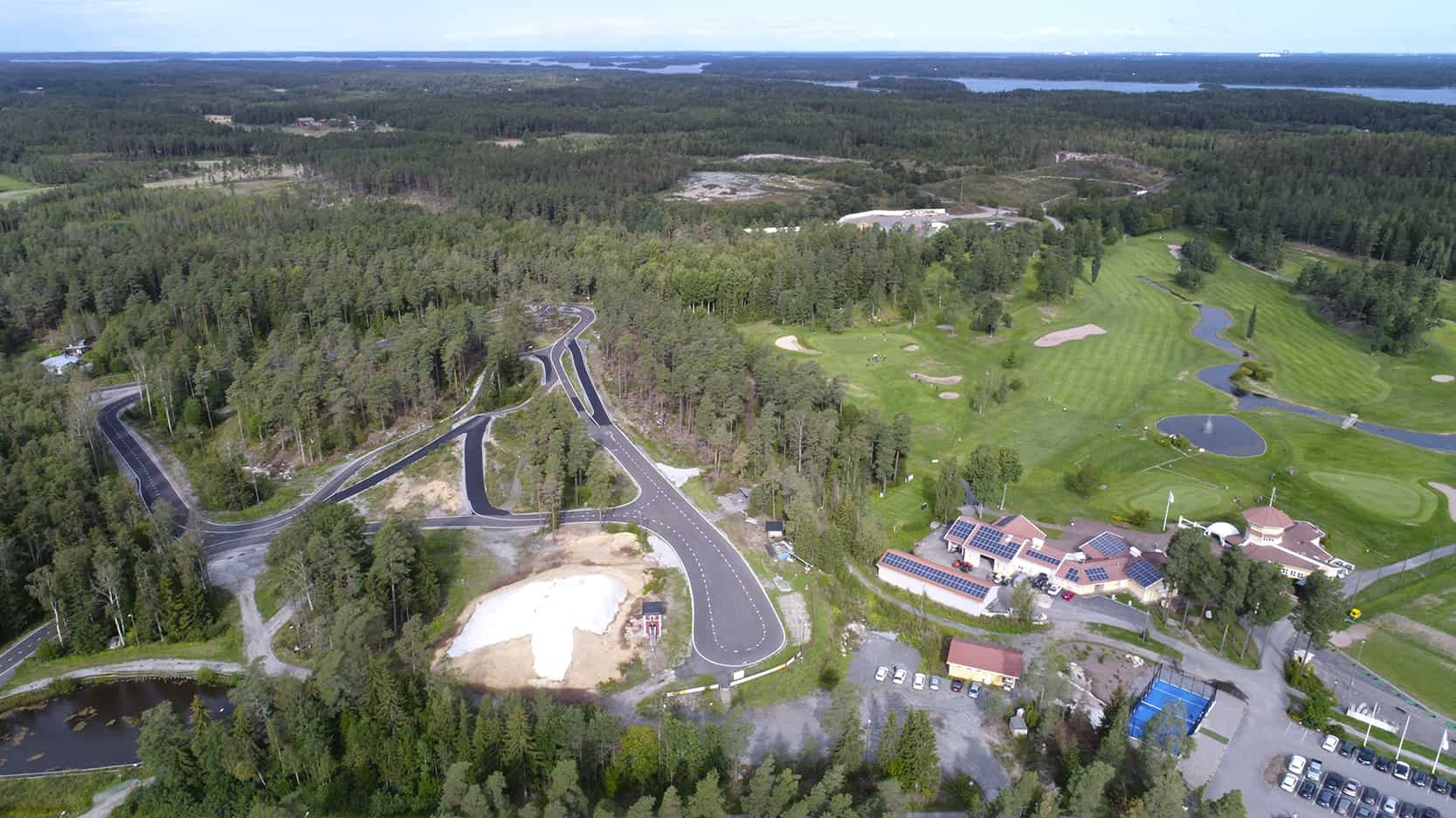 Ilmakuvassa näkyy vasemmalla rullahiihtorata ja oikealla golfkenttä, väliin jää sinipohjainen padel-kenttä.