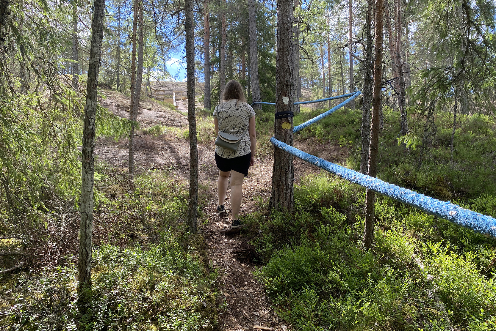 Nainen nousee rinnettä ylös sininen köysi oikella puolellaan.