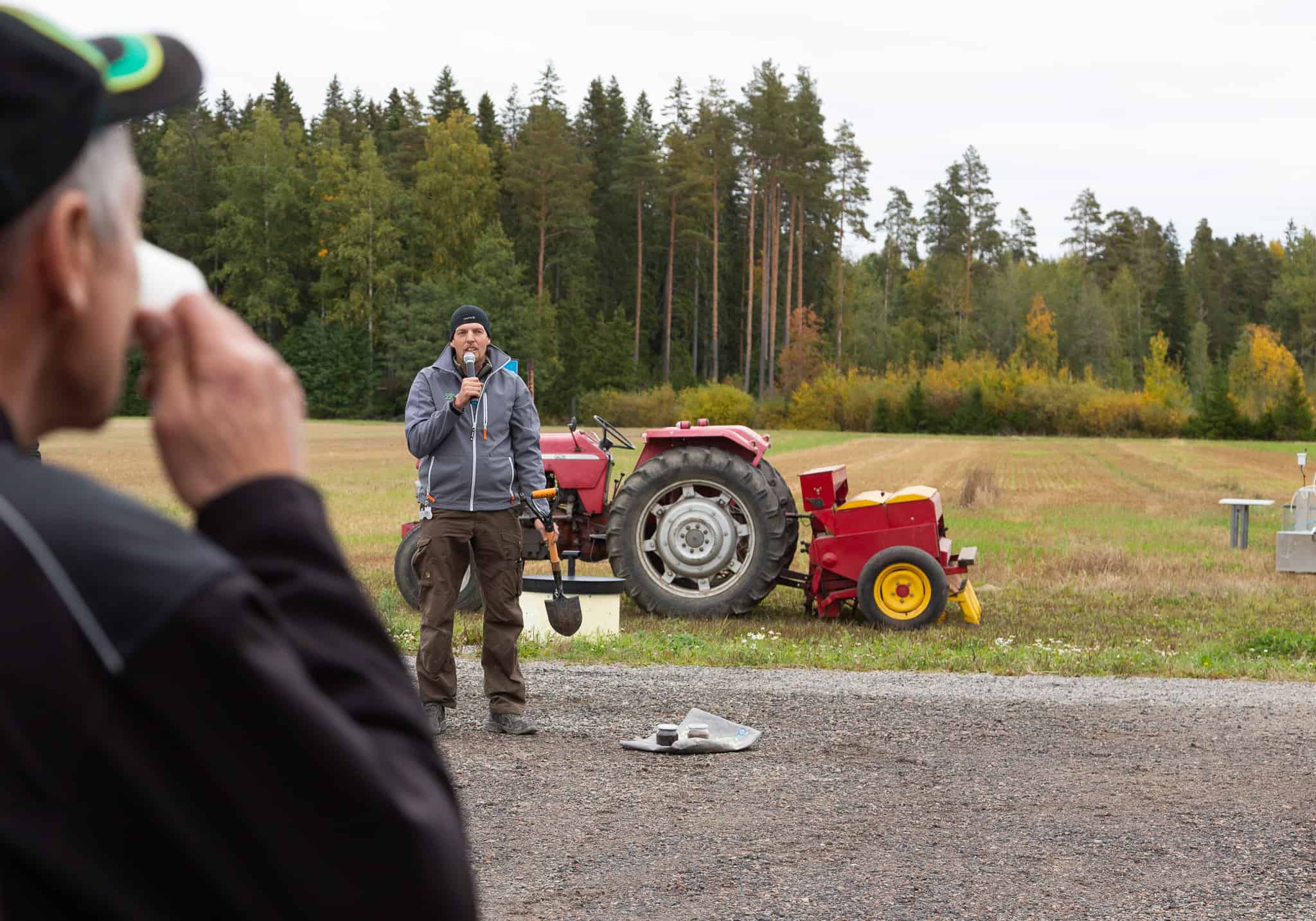 Mies puhuu mikrofoniin traktorin edessä pellon reunalla.