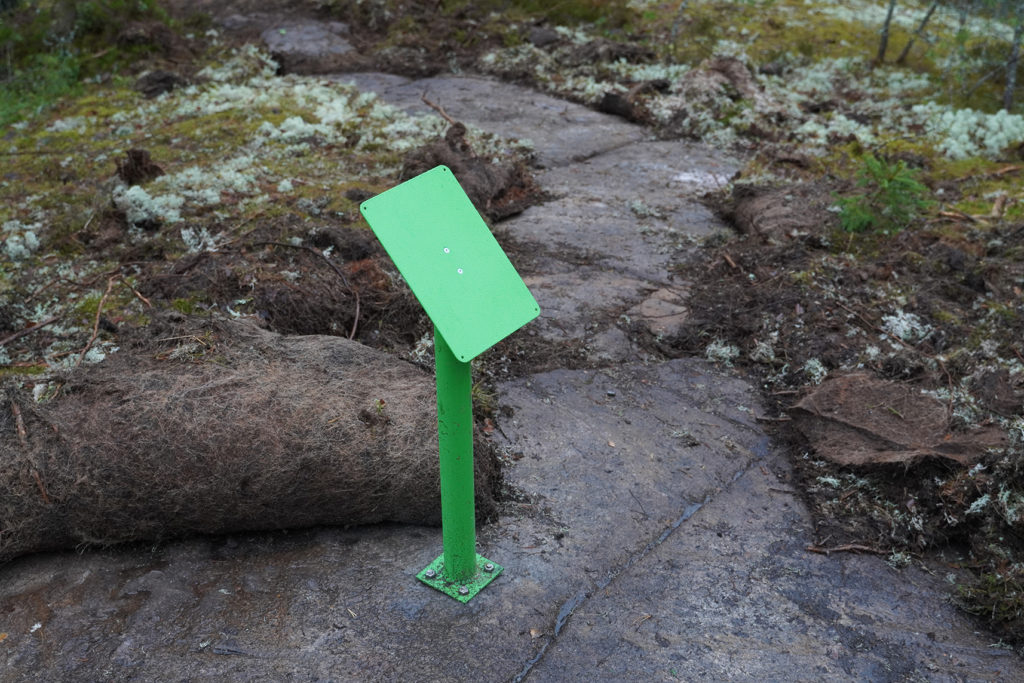 Vihreä opaskyltti kalliolla, jonka päältä on kääritty maaperäkerros pois.