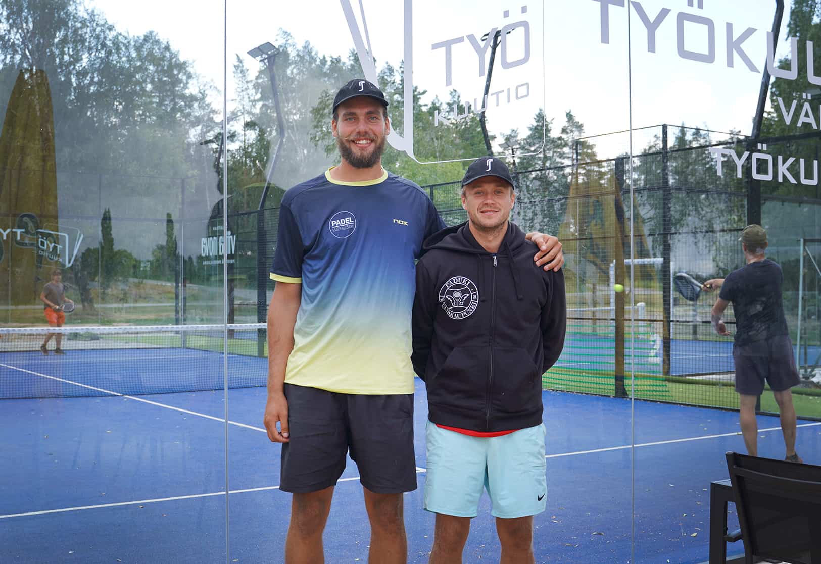 Mikeael ja Georg seisovat vierekkäin Pade Uusikaupunki Oy:n paidoissa padel-kenttien edessä.