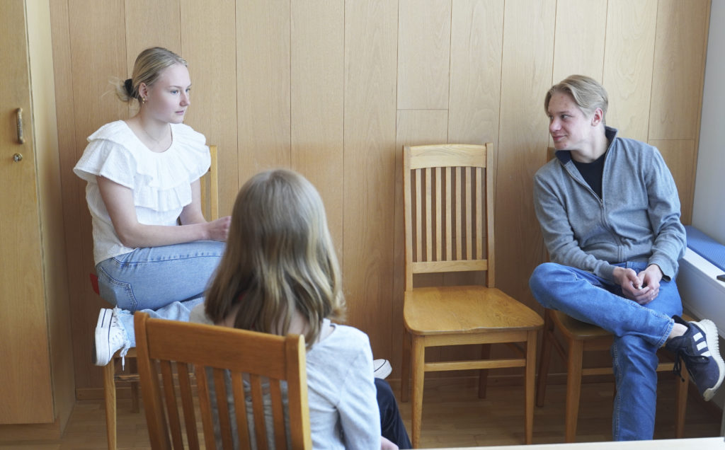 Kolme nuorta keskustelee huoneessa.